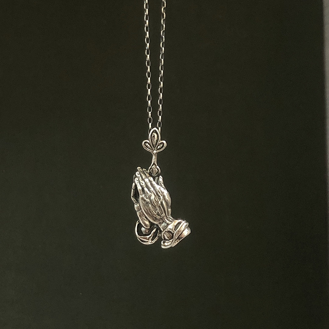 Collar de plata detallado / manos de oración